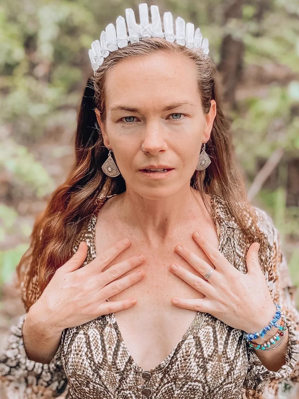 Erin Frances wearing a crystal crown, hands resting on her heart in the forest at Ilkley Haven